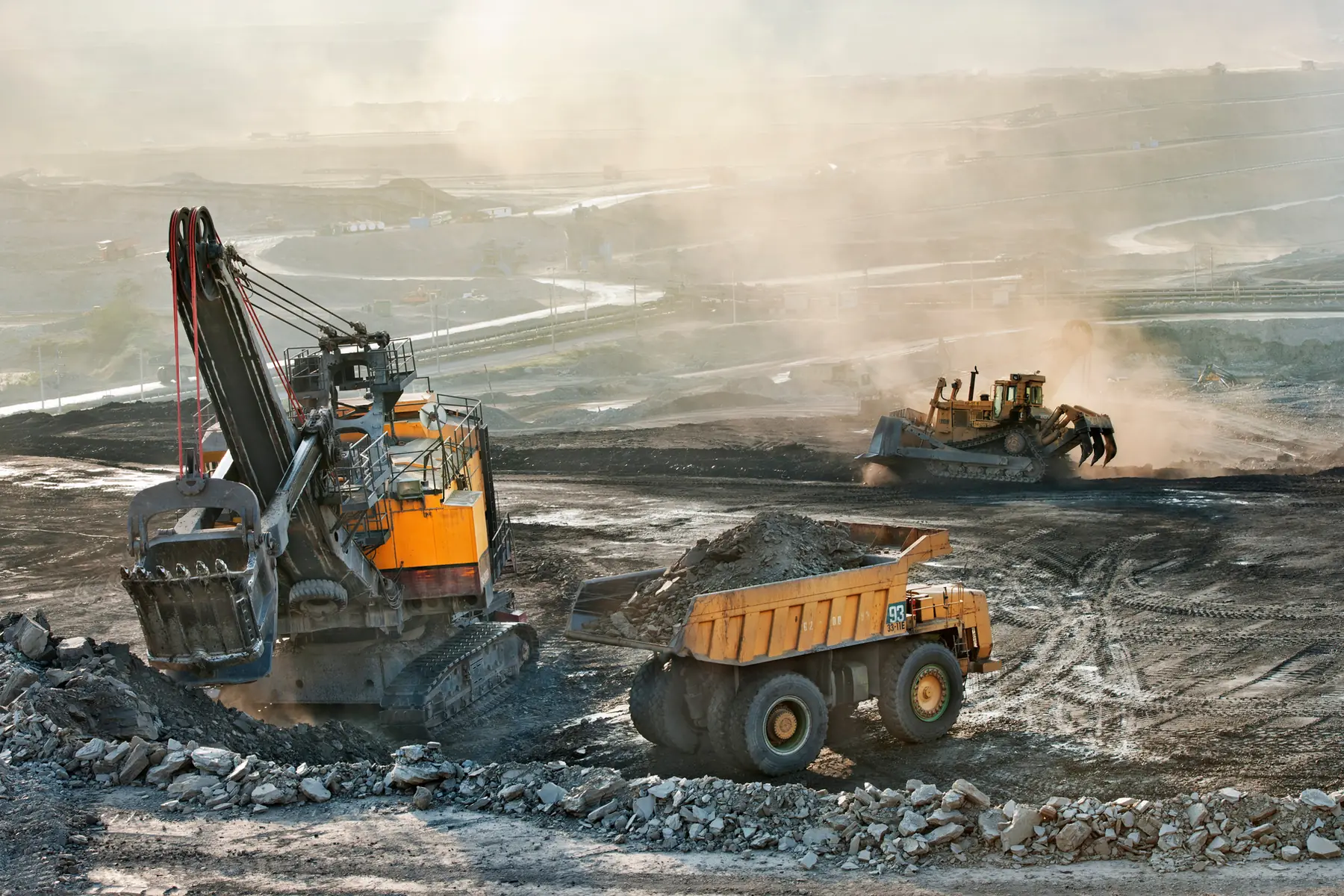Excavator loading a haul truck at a dusty open-pit mine